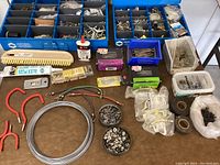 Top view of table with two blue plastic compartment boxes filled with assorted screws, nuts, hooks, bolts, and other hardware items, plus loose tools and components on surface.