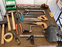 Overview of multiple hand tools on brown table including hammers, pliers, handsaws, tape, screwdriver, and measuring tools