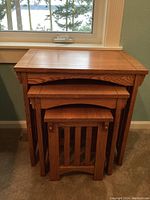 Front view of the three oak nesting tables nested together, showing their relative sizes and design details including slatted side panels on the smallest table.