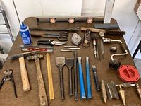 Tools arranged on a table including levels, chisels, hammer, scissors, brace drill, and a chalk line reel.