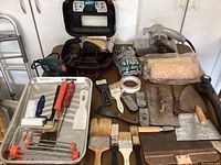Overview of the lot showing power sanders, brushes, paint rollers, scrapers, trowels, and paint trays arranged on table.