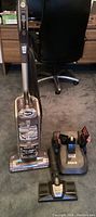 Front view of Shark Rotator vacuum with powered brush head and charging dock with attachments on carpeted floor.