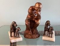 Front view of three statues; The Thinker bronze-colored statuette in center flanked by two dog bookends on marble bases