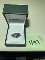 Front view of ring in green hinged jewelry box showing pear-shaped blue topaz and clear accent stones