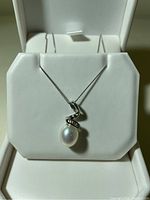 Front view of the pearl pendant hanging from the white gold chain placed on a white jewelry display stand inside a jewelry box.
