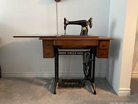 Front view of the Singer treadle sewing machine mounted on the wooden cabinet with drawers visible and cast iron base.