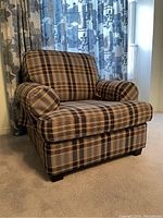Front view of plaid upholstered armchair with rolled arms and short wooden legs on carpeted floor.