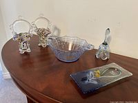 Full view of five-piece blue and clear art glass collection featuring two baskets, bowl, bell, and spoon rest on wood tabletop