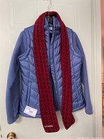 Blue Columbia insulated vest with fleece sleeves and red and black houndstooth fleece scarf hanging on a hanger