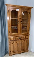 Full view of wooden corner hutch with glass doors and closed lower cabinets