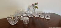 Wide view of crystal decanter, six whiskey glasses, two crystal bowls and decorative flower on wooden table