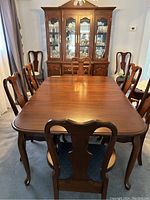 Front view of the wooden dining table with eight chairs around it and a china cabinet in the background.