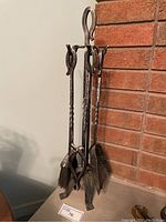 Full view of the metal fireplace tool set standing on a surface in front of a brick fireplace, showing all tools and stand.