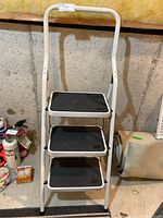 Front view of the 4-foot folding step ladder with three black steps and white frame.