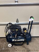Blue Mastercraft air compressor showing overall unit with coiled black hose and wheels, positioned in front of garage door.