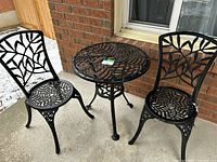 Full view of black metal bistro set on concrete patio, including round table and two chairs