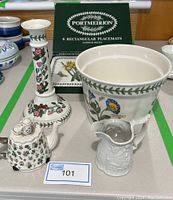 Overview of pottery items including candlestick with pink floral design, flower pot with blue flowers and green leaf border, white milk jug with embossed flowers, small porcelain teapot with floral pattern, and box of Portmeirion rectangular placemats