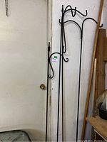 Four metal garden shepherd's hooks leaning against a wall near a door. Various hook designs visible at the top.