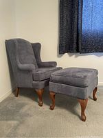 Gray Sklar-Peppler armchair with matching ottoman in a carpeted room near a window with dark curtains.