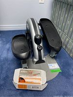 Stamina In Motion exerciser showing black foot pedals and resistance knob with Tempo weight box in front.