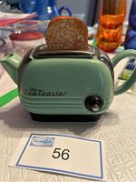 Front view of teal ceramic Teapottery toaster-shaped teapot with one toast-shaped lid piece inserted and black knob detail.