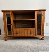 Front view of TV stand showing overall structure, cabinet doors, center shelf, drawer and bun feet
