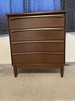 Front view of four drawer mid-century modern style dresser with dark walnut veneer finish and tapered legs