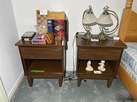 Pair of vintage MCM side tables with one having various decorative and household items on top and inside the open shelf, shown in a bedroom setting.