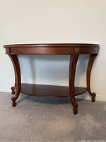 Front view of wooden half-moon shaped hall table with curved carved legs and lower shelf.