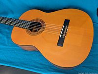 Close-up of the guitar body showing natural wood finish, black bridge with an ornate inlay, and six nylon strings.