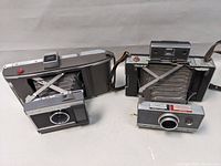 Two vintage Polaroid Land Cameras open showing bellows and lens area, left is Model J66 and right is Automatic 100.