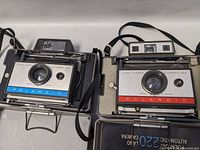 Two Polaroid Land Cameras, model 210 and 220, side by side showing front design and lens area.