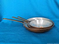Three copper skillets stacked, showing side profile and handles