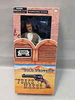 Front of the box displaying the toy figure visible through window, featuring western saloon doors graphics and revolver illustration labeled 'Peacemaker'