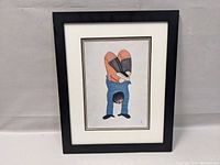 Framed Indigenous art print showing the full image of a person in a blue top doing a handstand with legs bent and crossed, framed in a black frame.