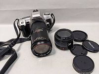 Photo showing Minolta Maxxum HTSi camera with 75-200mm zoom lens attached, alongside additional 50mm lens and lens caps.