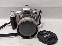 Front view of Nikon N55 SLR camera with attached lens and Nikon lens cap placed beside the camera.
