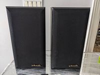 Front view of both bookshelf speakers with black fabric grills on, showing intact gold 'polk audio' badges on bottom right corner of each grill.