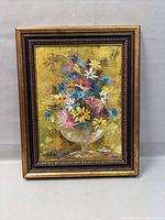 Framed oil painting showing vibrant floral still life with thick impasto texture in a gold and brown carved frame.