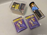 Photograph showing two sealed vintage Star Trek collectible card packs, a box of Star Trek cards, and a figure in a blue uniform inside a cylindrical case.