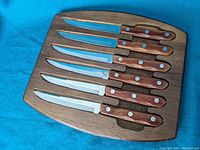 Six serrated knives with wooden handles displayed in a custom wooden rack.