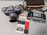 Overview photo showing Zeiss Ikon Contaflex camera with lens and rubber hood, quick film pack cartridge, Zeiss Ikon Contaflex manual, and brown leather camera case with shoulder strap.