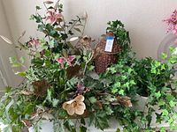 Photo showing the assortment of artificial plants including green ivy and pink flowers next to a wicker birdhouse.