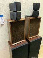 Medium and larger speakers stacked in pairs showing wood frames and fabric covers with black larger speakers below.