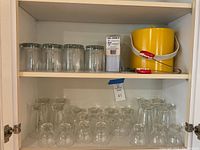 Clear glassware arranged on lower two shelves including large, medium, and shot glasses. Top shelf shows unopened package of stirrer straws, yellow ice bucket, and teeth-shaped tongs.
