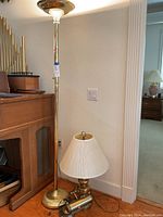 Brass torchiere floor lamp and brass table lamp with white pleated shade positioned near a piano.
