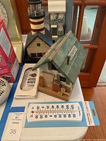 Green and beige decorative bird house with white outdoor thermometer in packaging on table