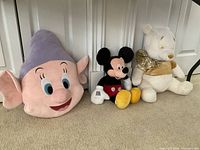 Photo of three Disney plush dolls showing Dopey on the left, Mickey Mouse in the center, and Winnie the Pooh on the right.