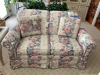 Front view of floral patterned loveseat with two matching cushions, showing fabric and design details.