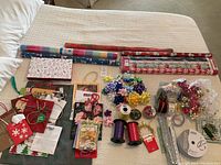 Wide view of gift wrapping supplies spread on a bed including wrapping paper, gift bags, bows, ribbons, and gift tags.